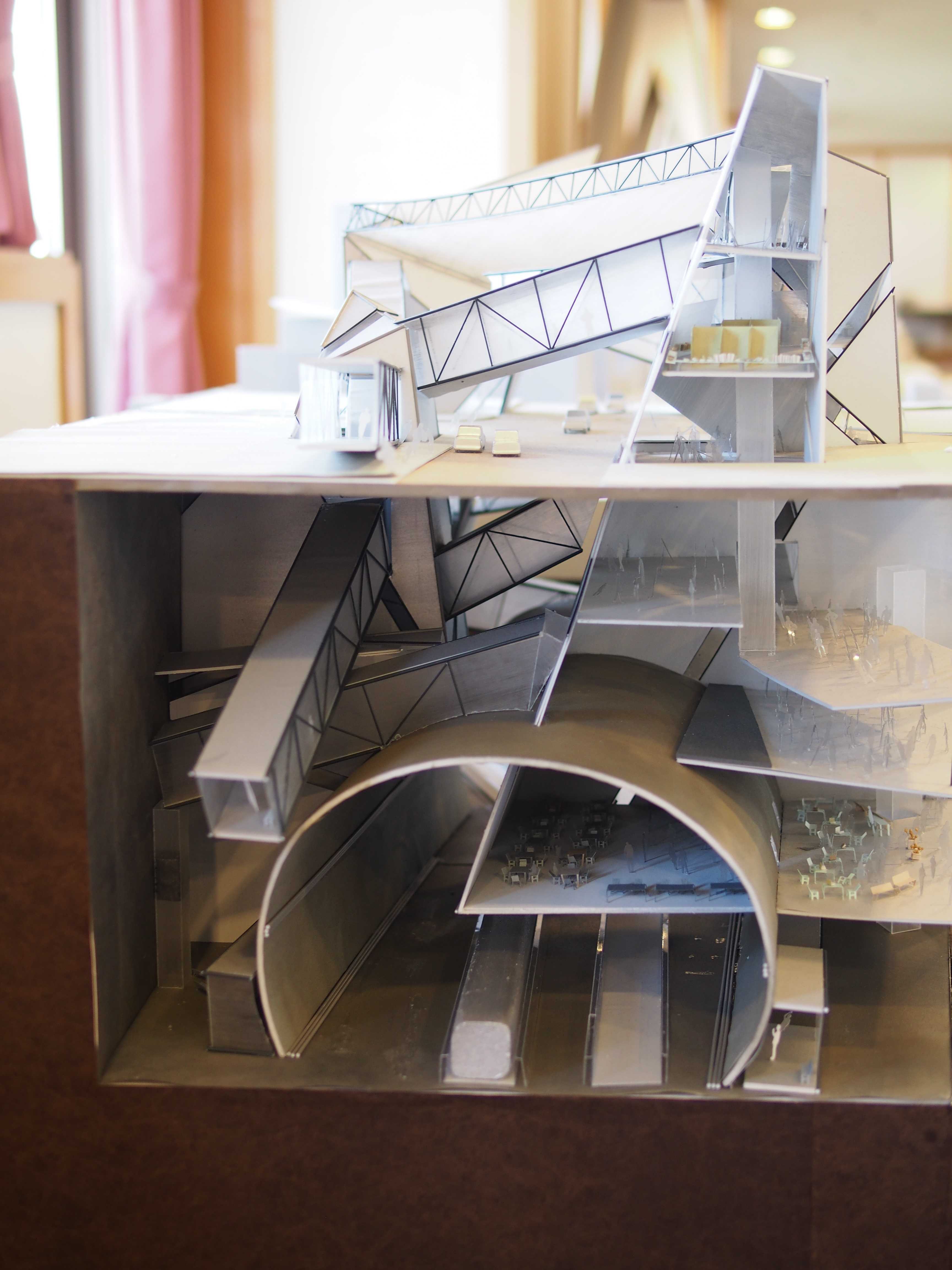 Cutaway architectural model showing a complex multi-level building interior with curved tunnel-like structures and miniature figures