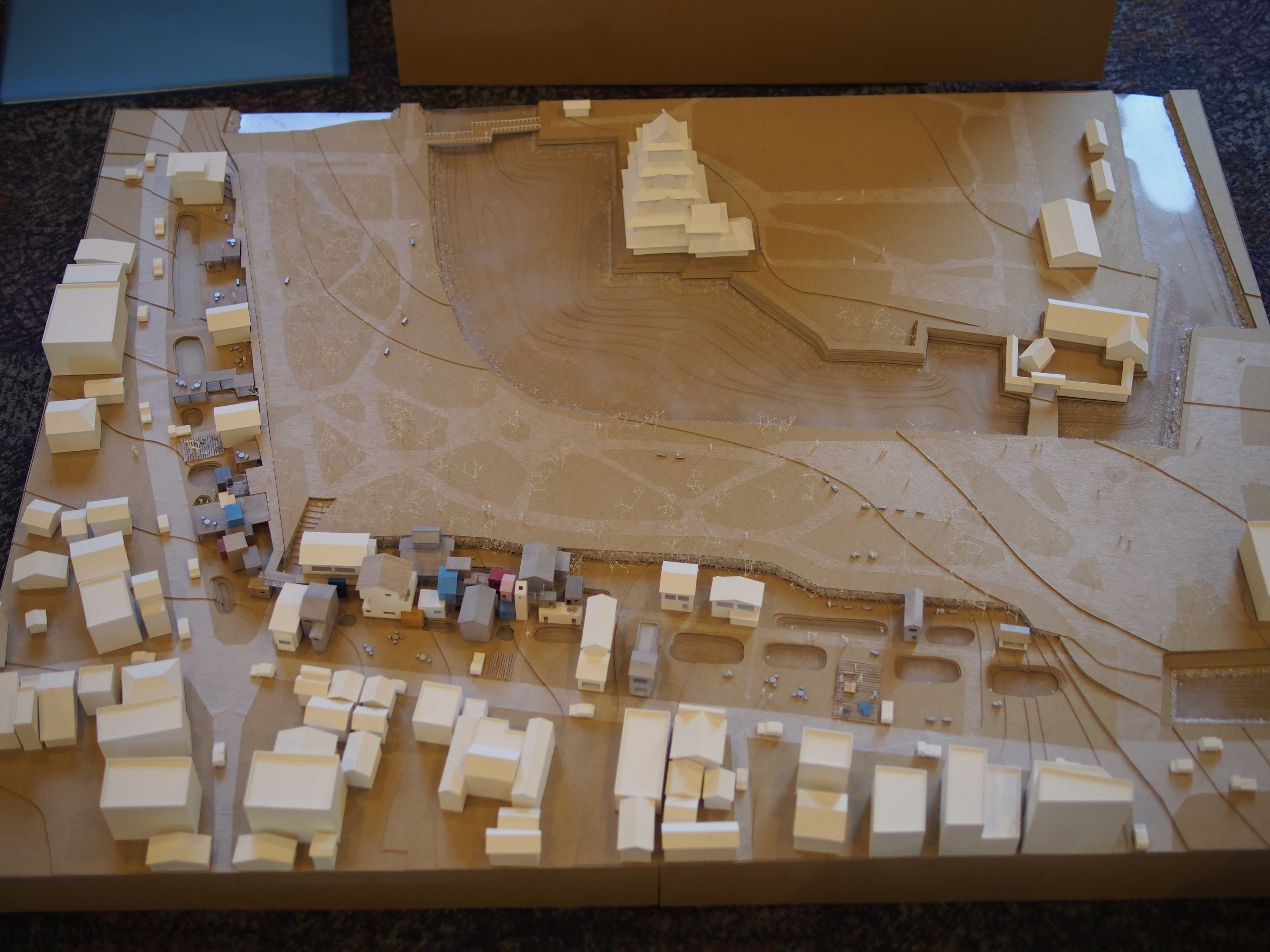 Architectural site model depicting a hilltop structure resembling a castle surrounded by pathways, greenery, and small buildings