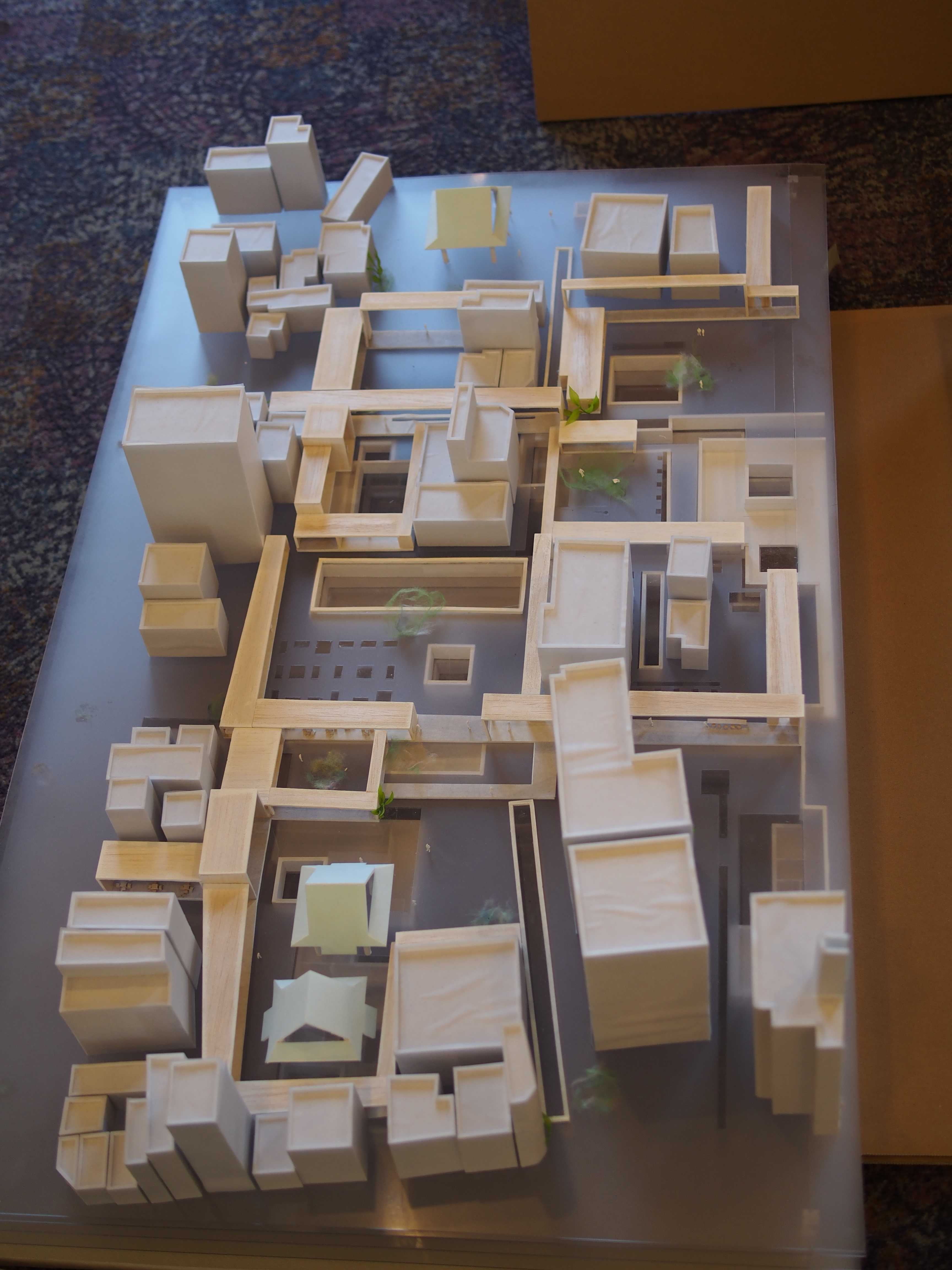 Overhead architectural model of a dense urban layout with white and beige block buildings representing streets and courtyards