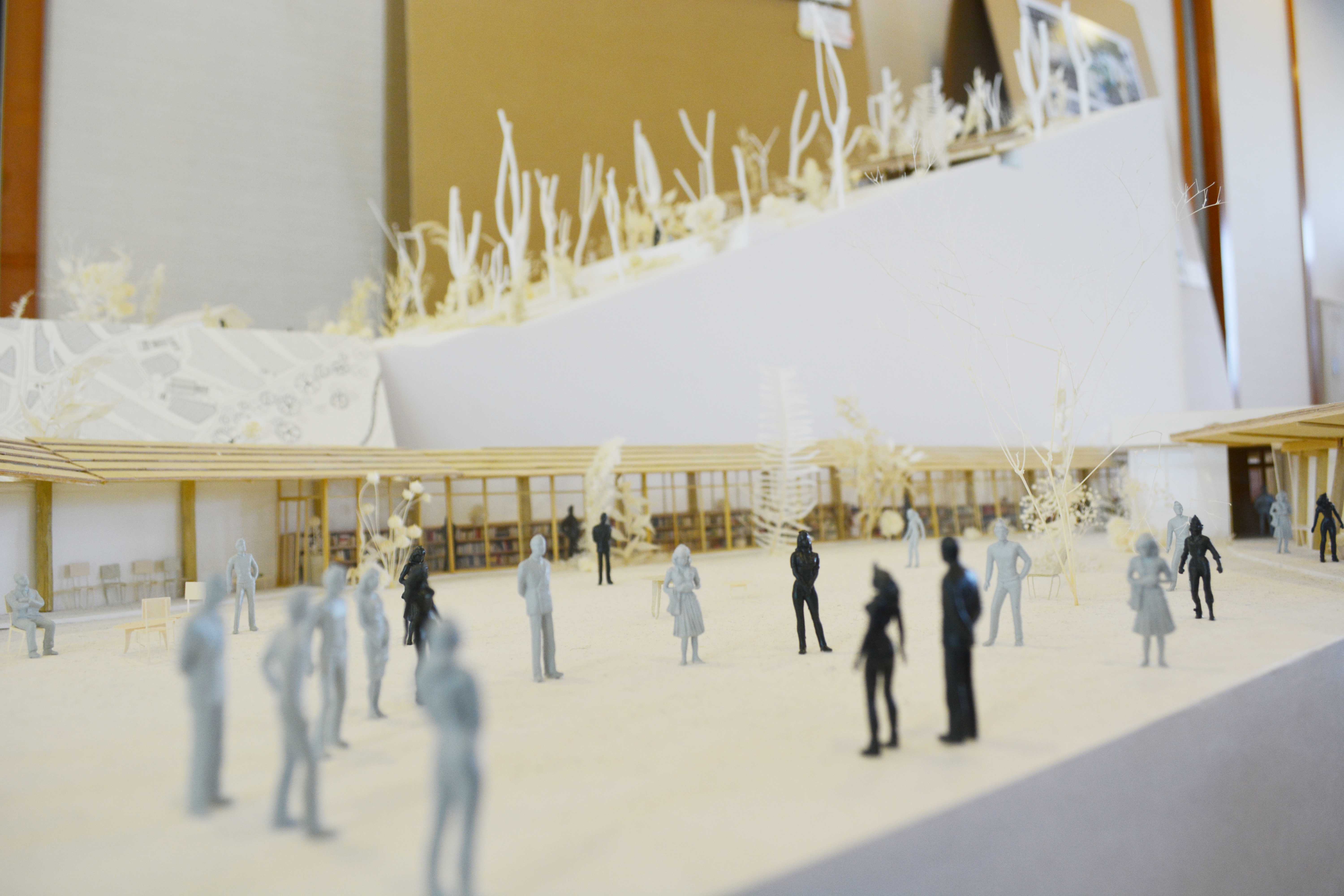 Architectural model of a building interior with tiny figurines standing on a light-colored floor, surrounded by structural elements