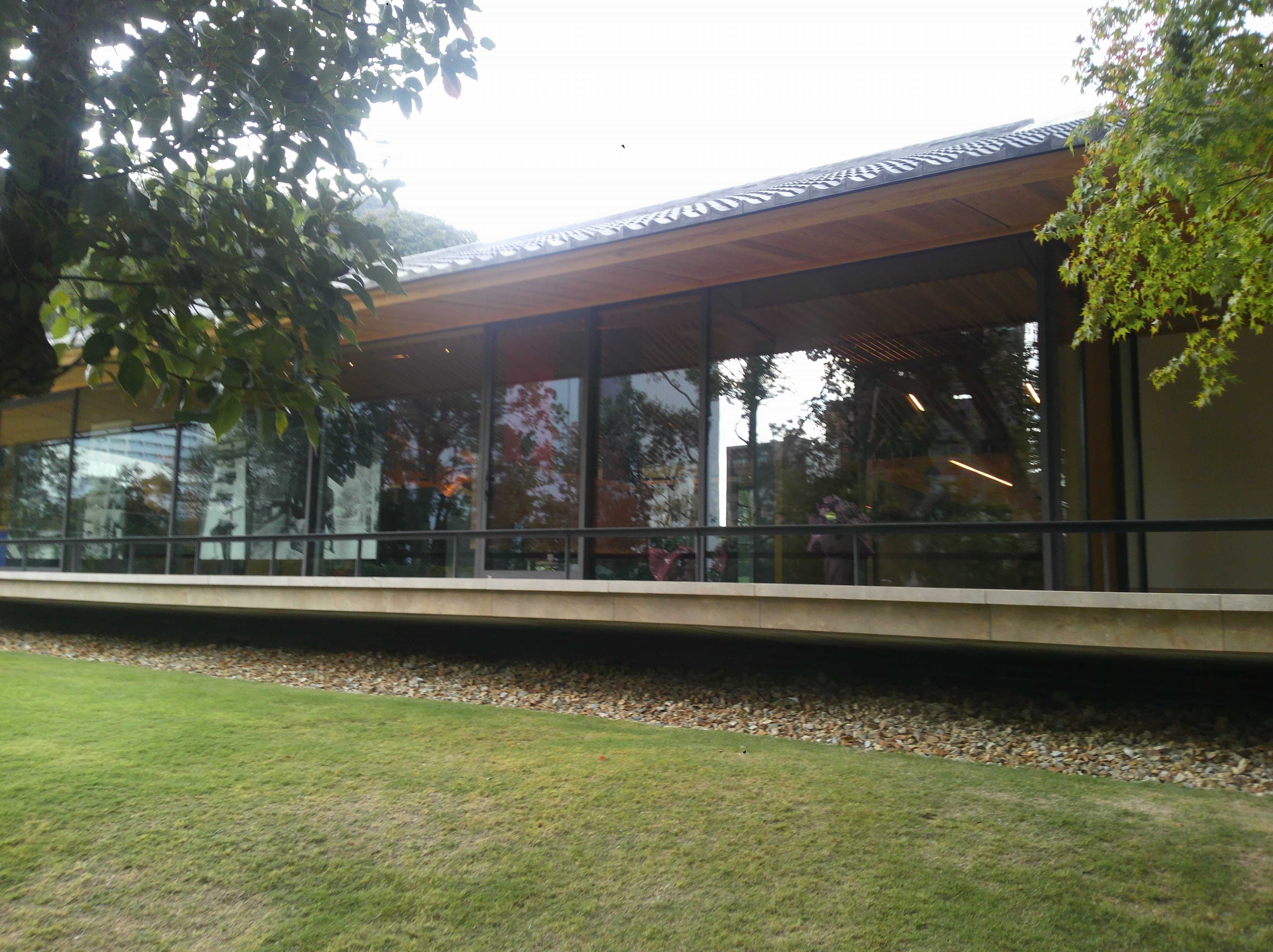Modern building exterior with a wide overhanging wooden roof, glass walls, and a lawn with gravel border in front