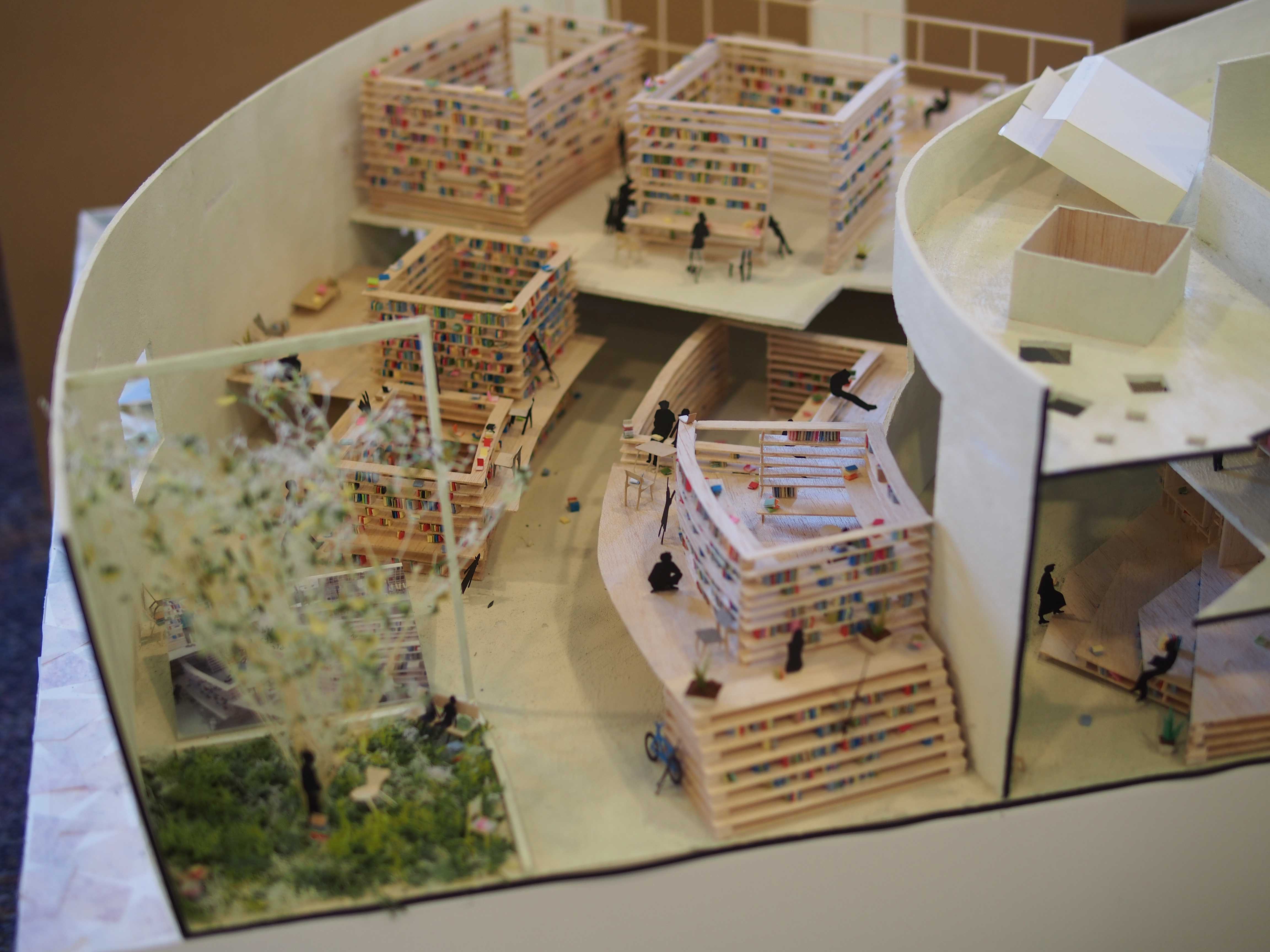 Detailed architectural model showing an interior library layout with bookshelf towers, small figures, and a miniature tree